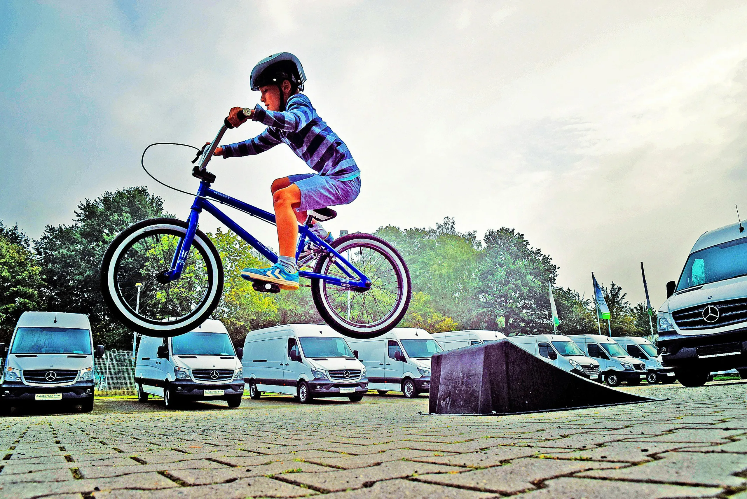 Young boy performing a BMX stunt at an outdoor parking area in Germany.