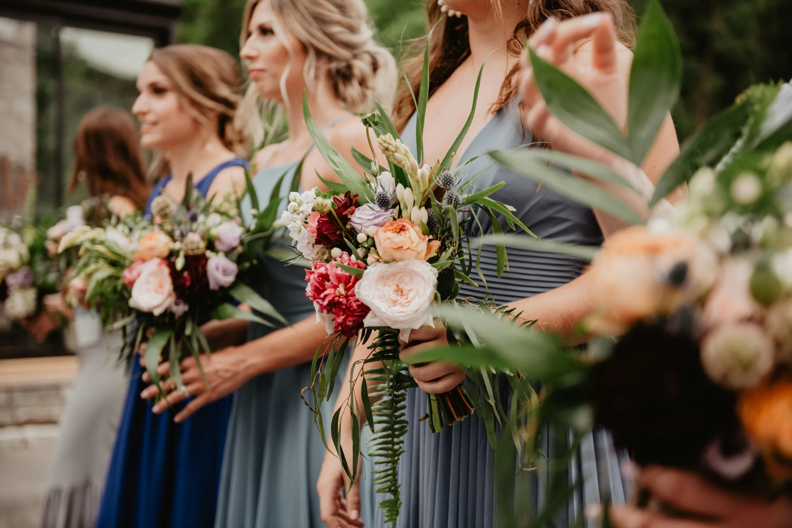 Bridesmaids in blue dresses holding vibrant bouquets during a wedding ceremony.