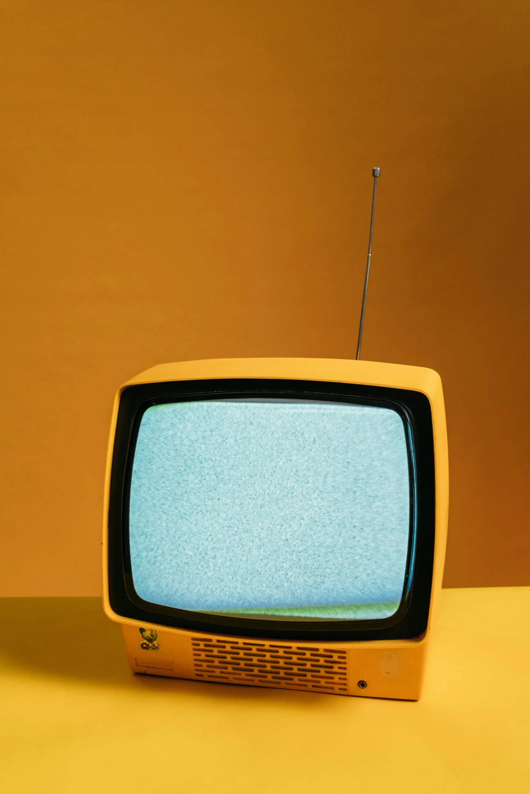 Retro yellow television on orange backdrop with static screen, perfect for vintage themes.